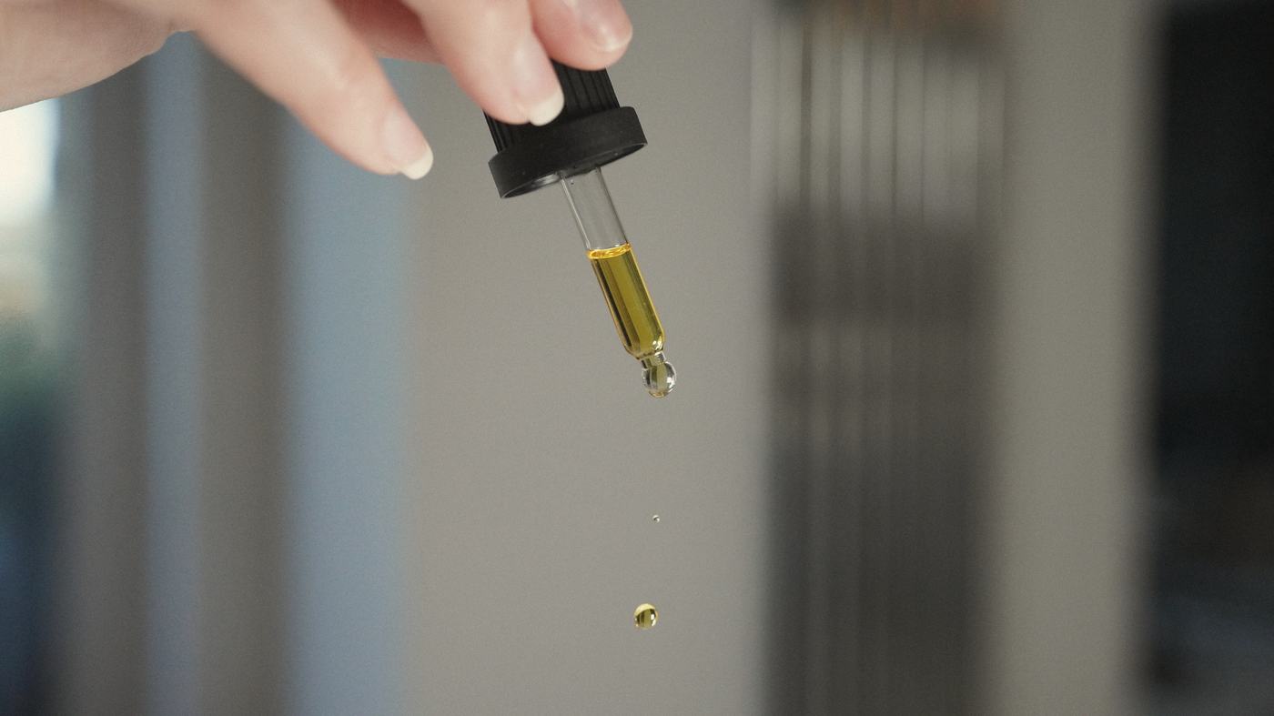 A hand releasing a single golden drop of oil from a glass dropper